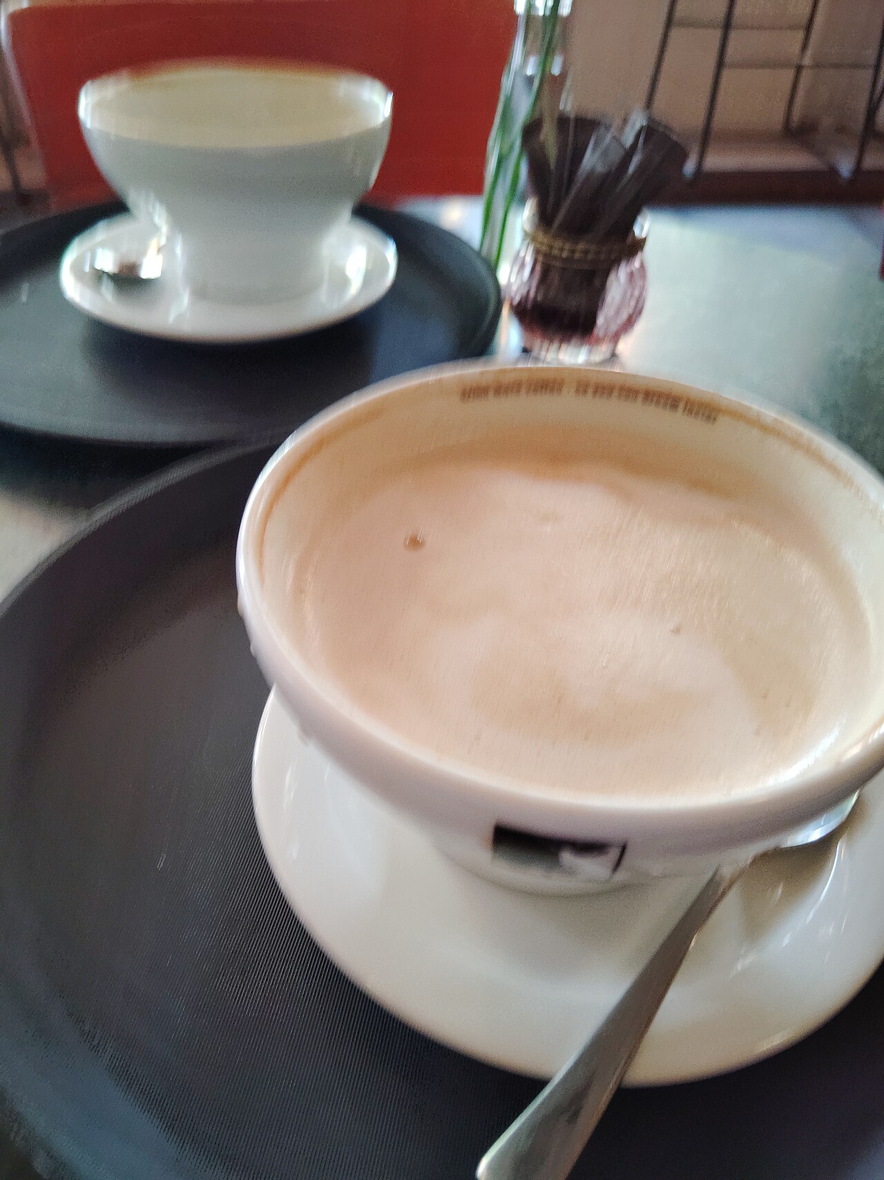 Pale café au lait in a white cup on a saucer, with a spoon.