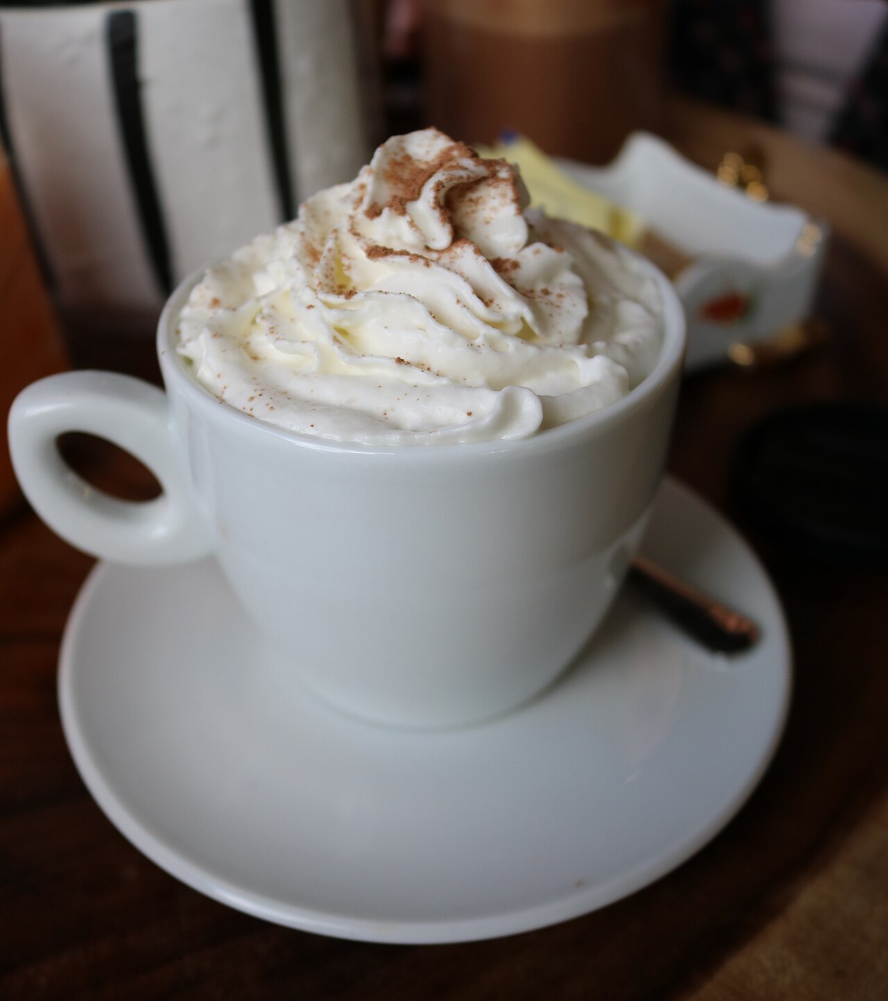 White cup topped with whipped cream and a fine brown dusting, on a saucer.