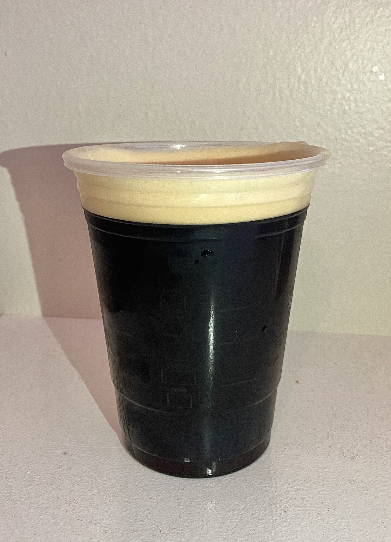 Dark nitro cold brew in a clear cup under a pale dense foam head.
