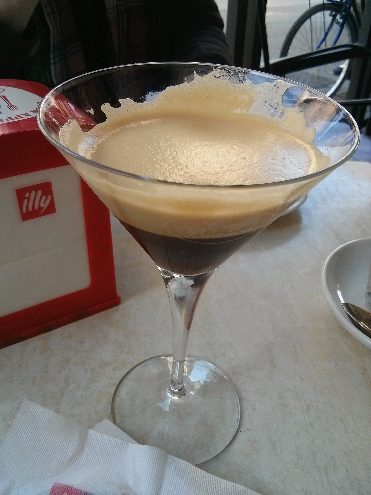 Foamy shakerato in a clear conical cocktail glass on a café table.