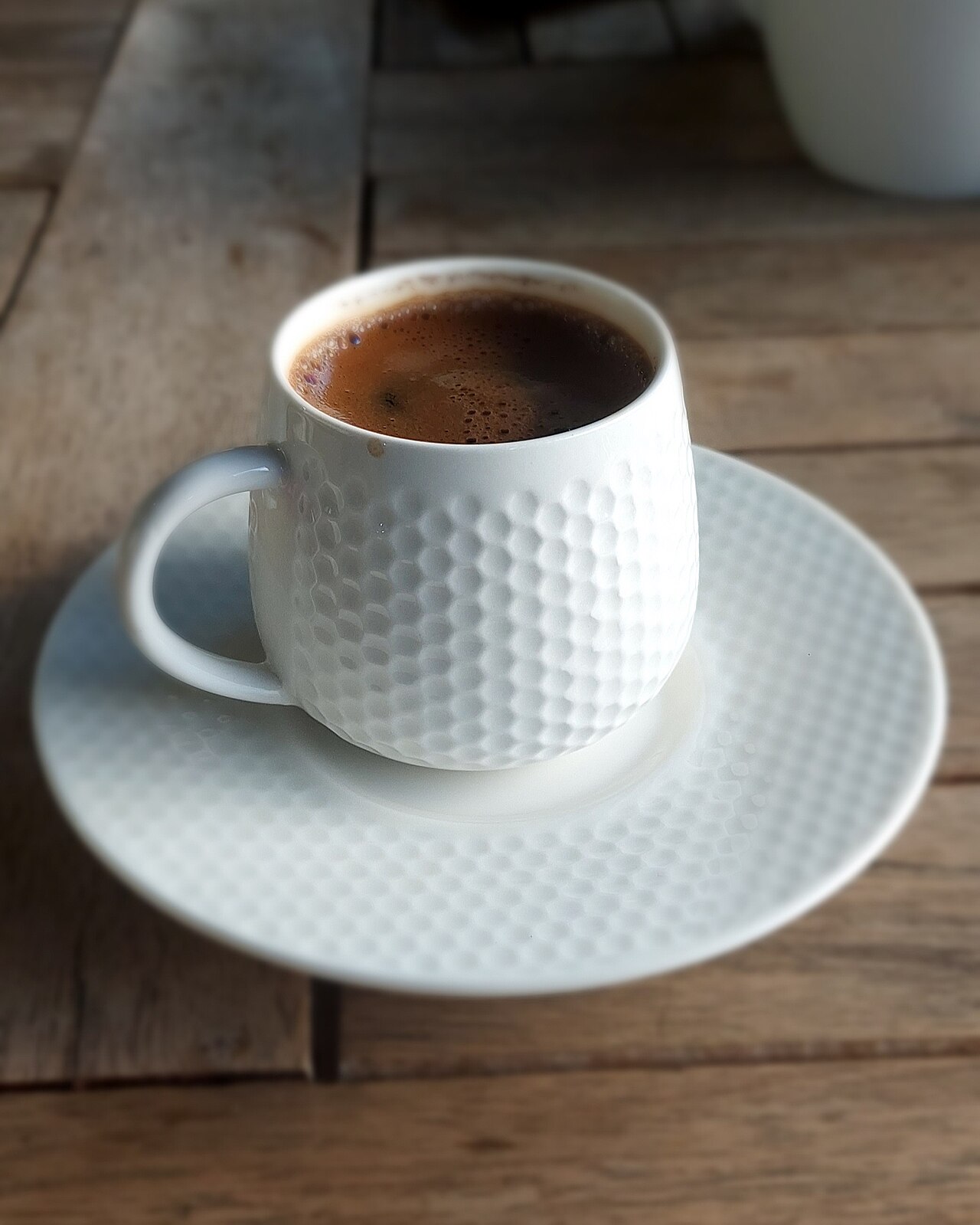 Dark Turkish coffee with a fine foam surface in a textured white cup and saucer.